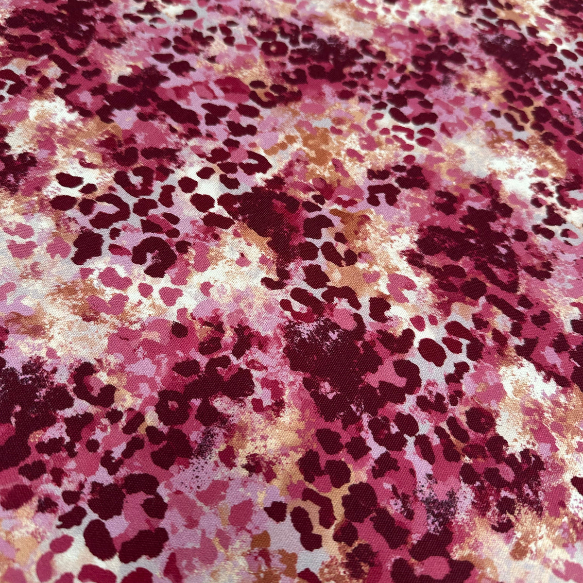 A close-up of a fabric or material surface with an abstract spotted pattern in pink, burgundy, golden cream, and tan.