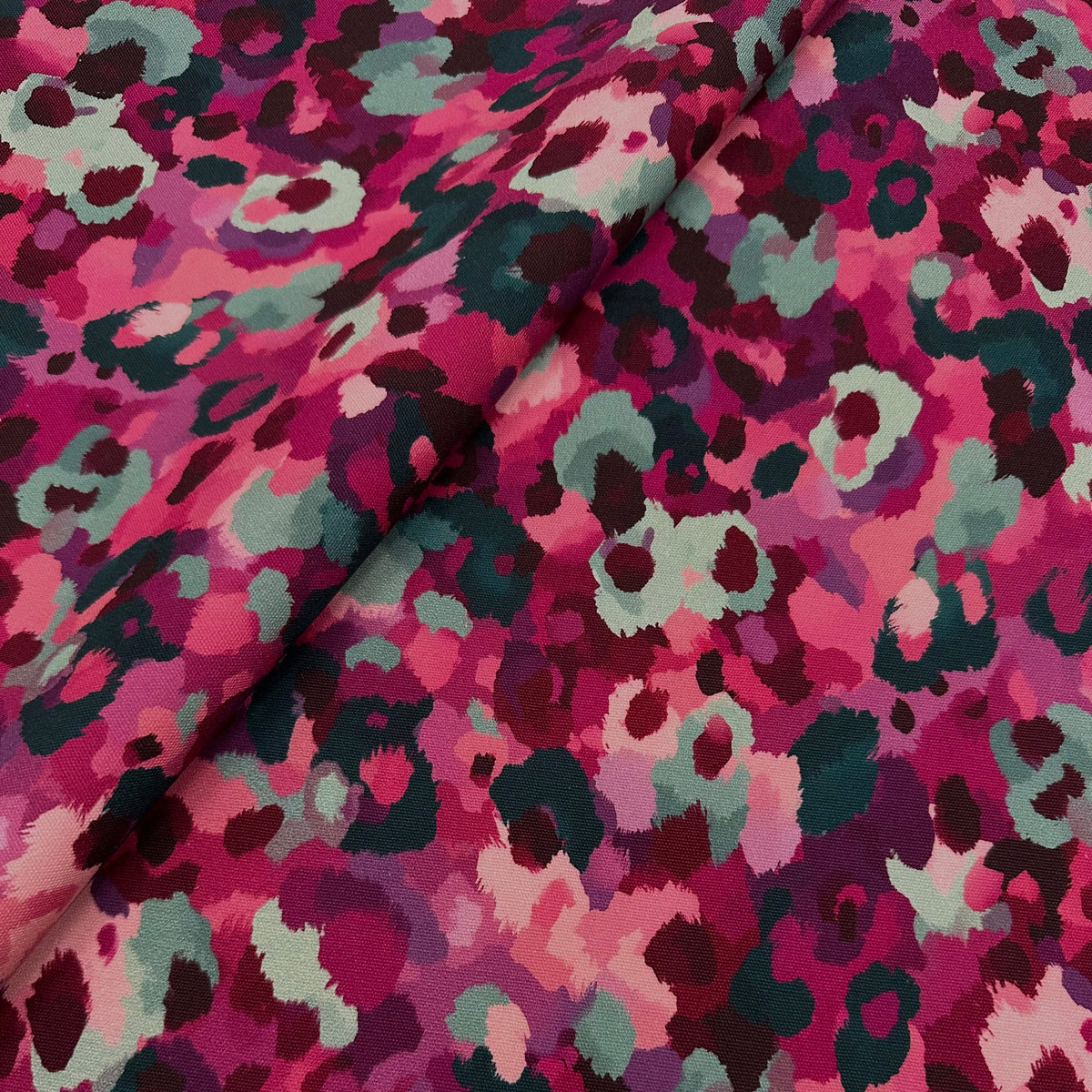 A close-up of patterned fabric with an abstract floral or watercolor-style print in pink, magenta, teal, and dark plum tones, draped with soft folds.