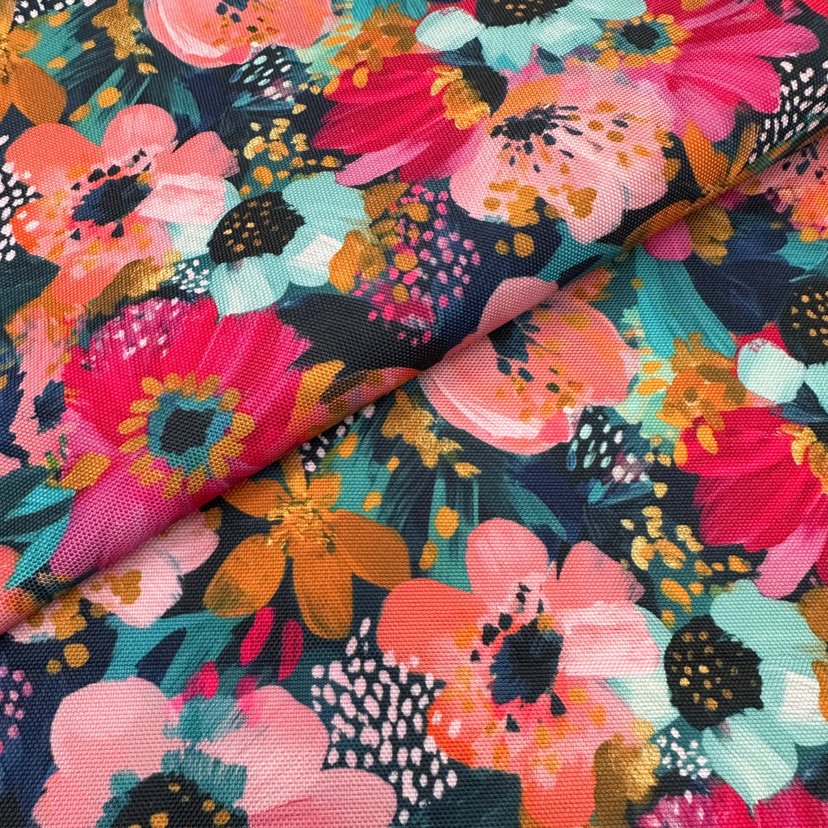 A close-up of a floral fabric with a bold, painterly pattern featuring pink, coral, teal, orange, and black flowers on a dark teal background.