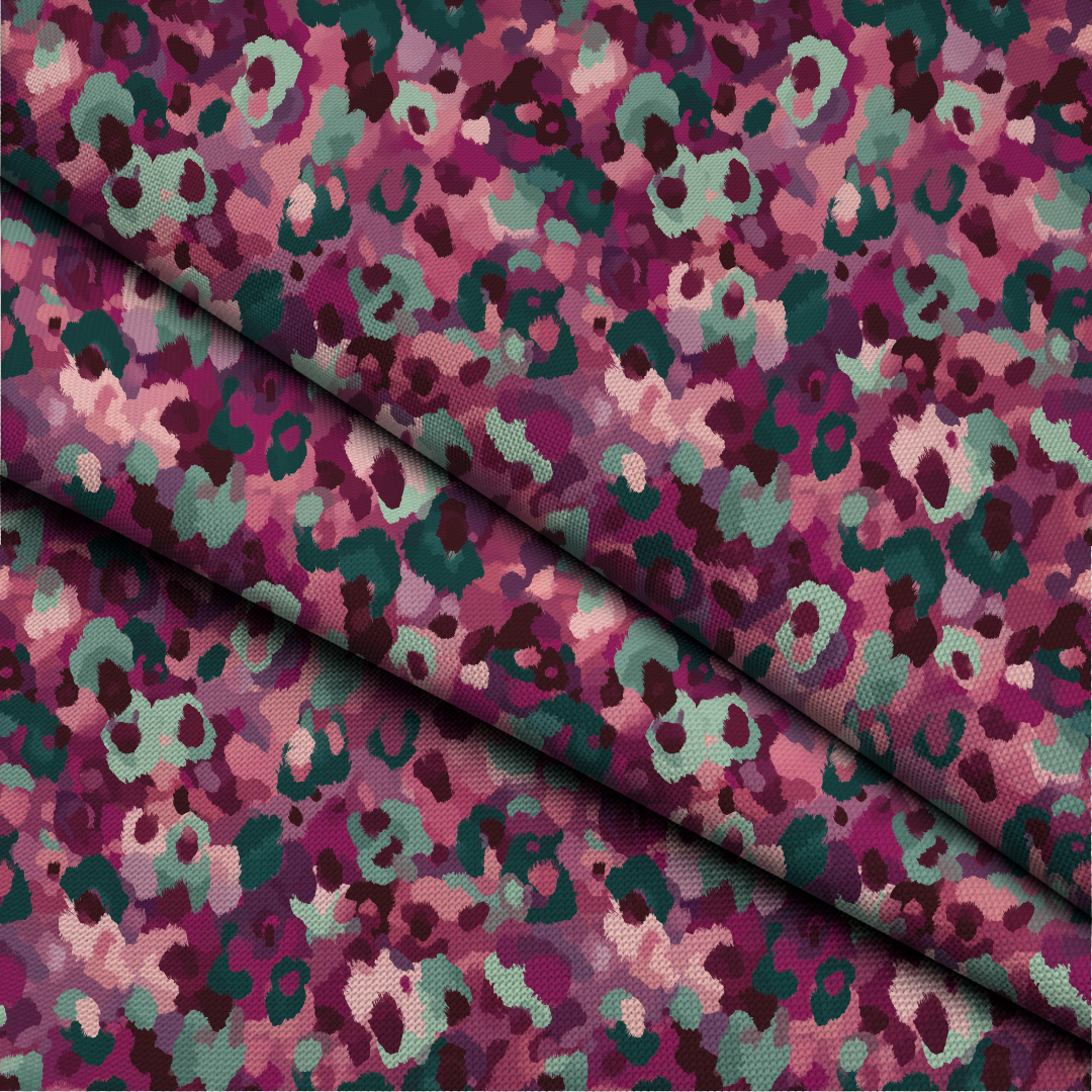 A close-up of patterned fabric with a camouflage-style abstract print in pink, purple, teal, and dark burgundy, folded diagonally across the frame.