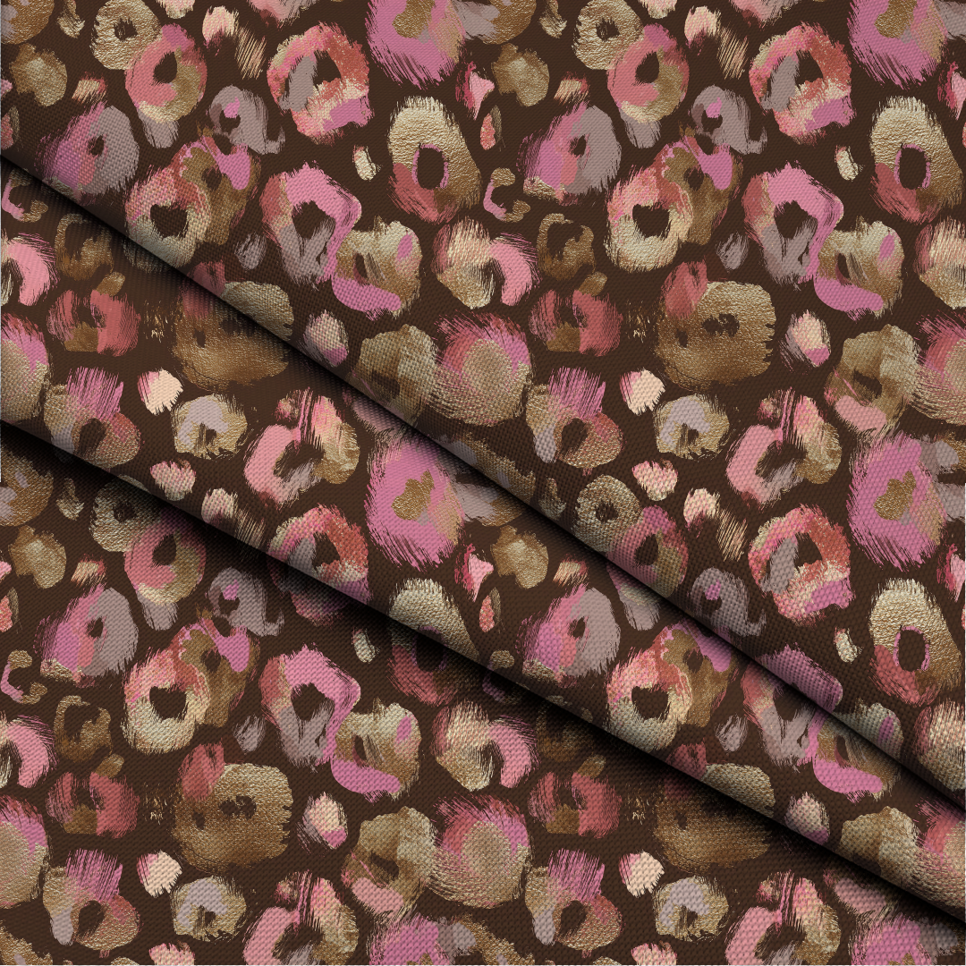A close-up of patterned fabric with a brown base and abstract leopard-like spots in pink, beige, and muted gold, arranged with one folded section creating a diagonal shadow.