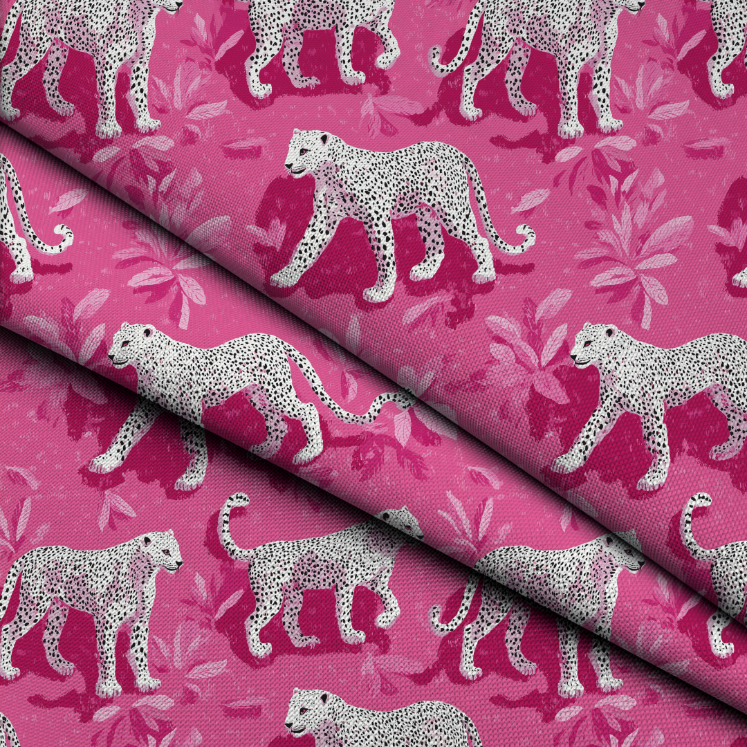 A close-up of folded pink fabric with a repeating print of white leopards and pale pink tropical leaves.