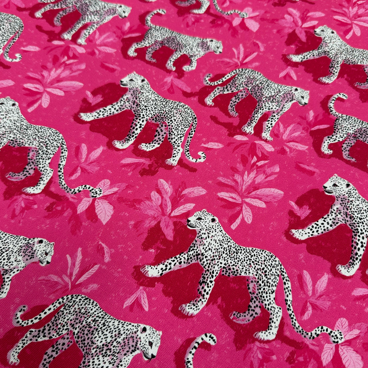 Bright pink fabric featuring a repeating pattern of white and black spotted leopards walking over a lighter pink floral background.